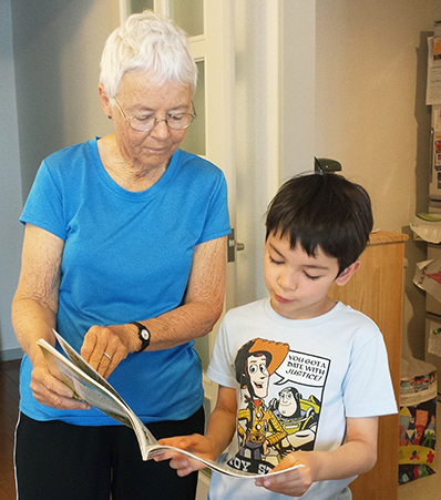 older adult standing and holding and showing a book to a child
