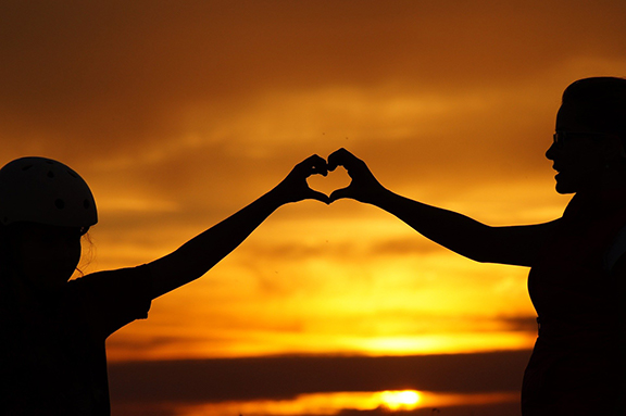 silhouette of two people connecting hands to form a heart