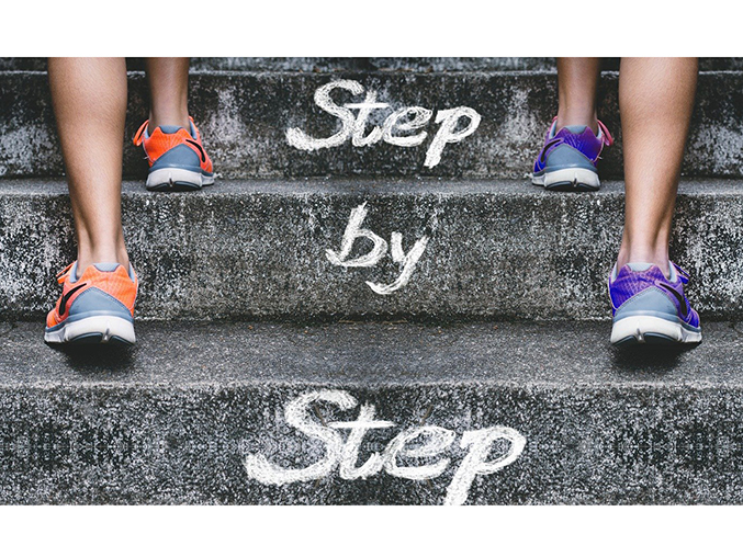 back of two people wearing athletic shoes walking up steps with words step by step