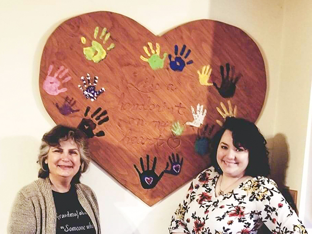 Cheryl and Charlotte standing in front of heart with handprints in paint