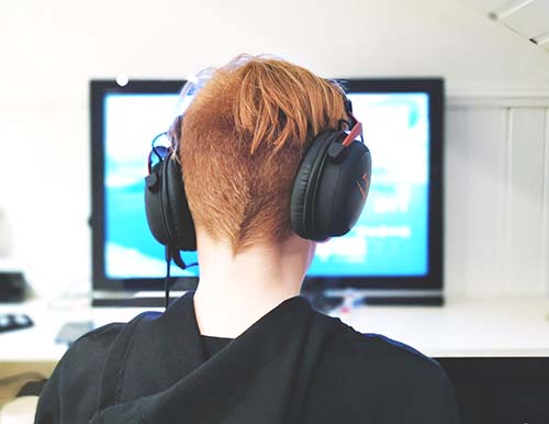 child wearing head phones looking at screen playing vdeo game