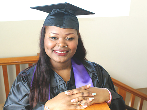 graduate with black cap and gown with purple stole