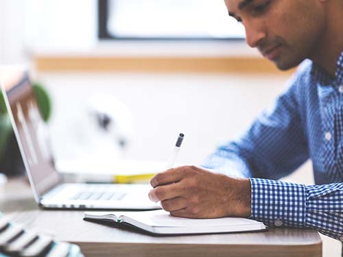 person sitting at table writing in notebook