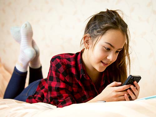 teenager laying on bed using cell phone