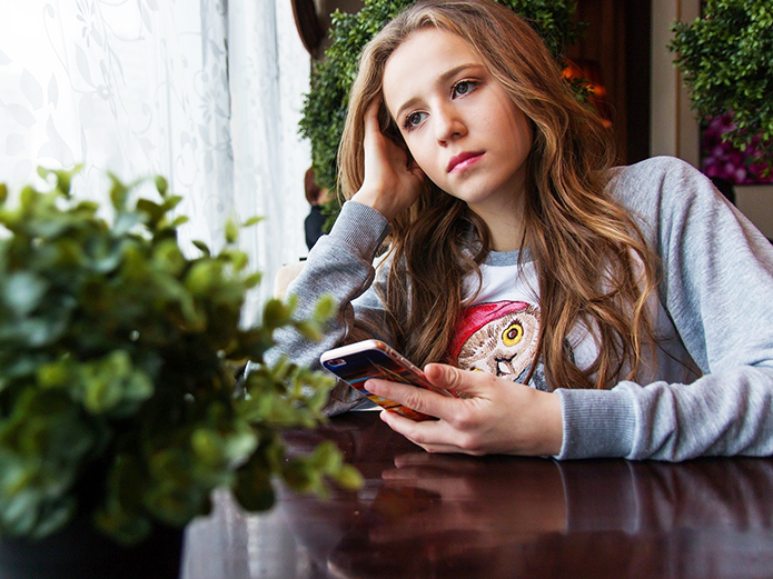teenager sitting looking out window holding cell phone
