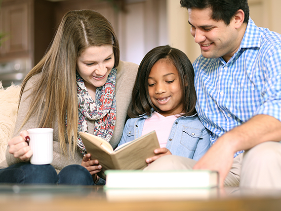 two adults and child in living room looking at book