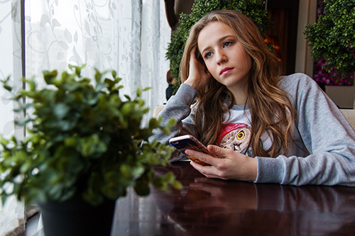 thoughtful girl alone at table with cell phone