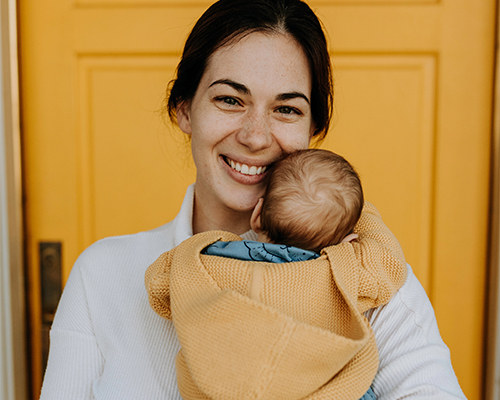 smiling woman holding baby in front of yellow door