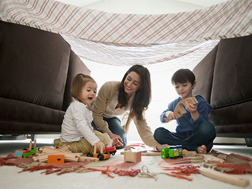 woman with girl and boy playing with trains under fort