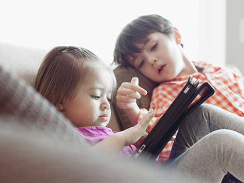 young boy and girl playing with tablet on couch
