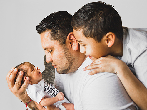 man smiling with older boy holding newborn