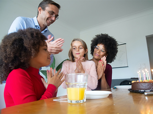 Man and woman with two girls in front of birthday cake with candles 