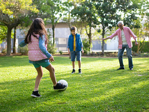 older man playing soccer with two children