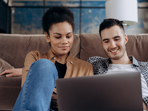 woman and man sitting on couch looking at laptop