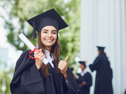 young woman in graduation cap and gown giving thumbs up 