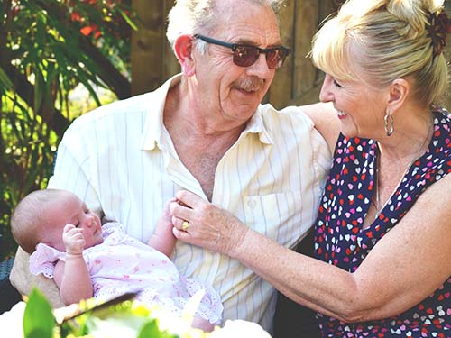 two older adults sitting outside holding baby