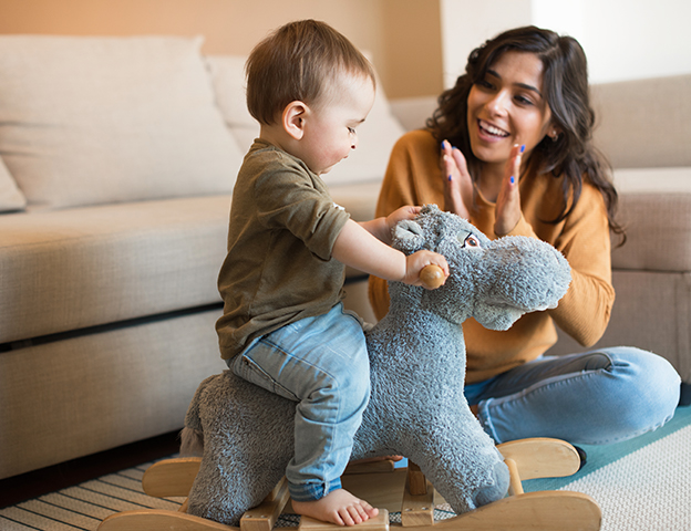 toddler riding wooden toy and mom sitting and clapping hands