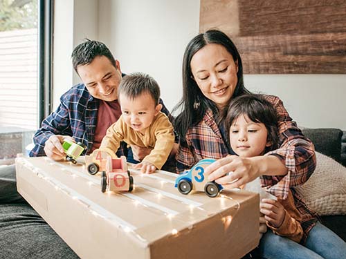 two parents and two young children playing with toy cars