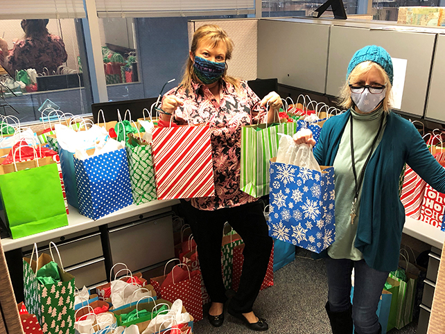 two people standing in cubicle holding gift bags