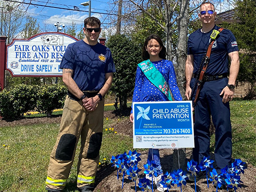 two firefighters and young girl standing in front of blue pinwheels