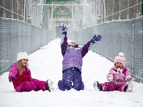 three children on bridge pathway playing in snow