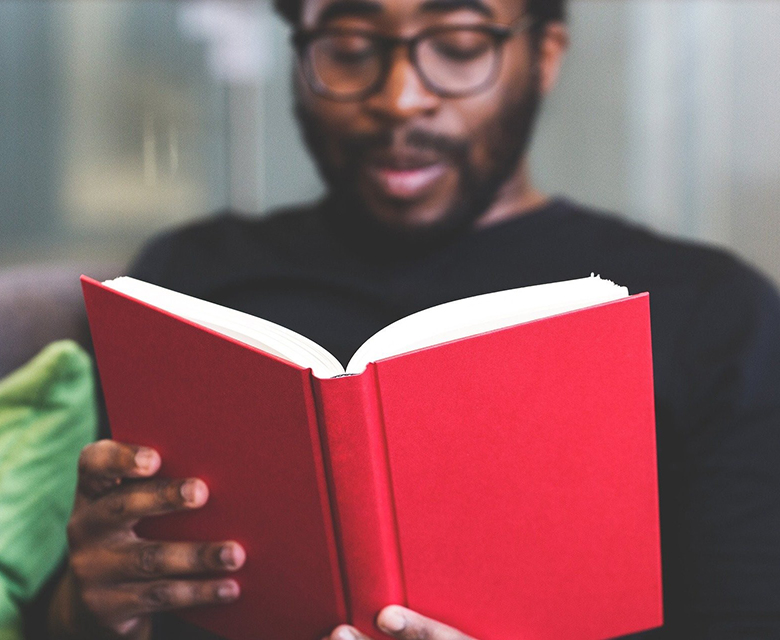 adult sitting reading red cover book