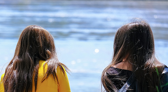 two people sitting side-by-side outside by the water