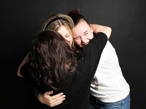three people smiling and hugging closely
