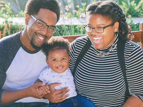 two parents sitting on park bench holding baby