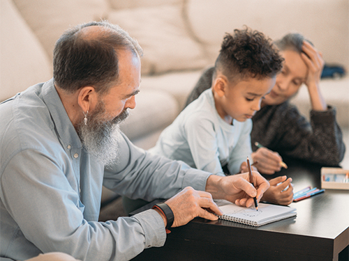 parents and child sitting at table writing