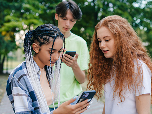 concerned girls looking at cell phone with boy behind them