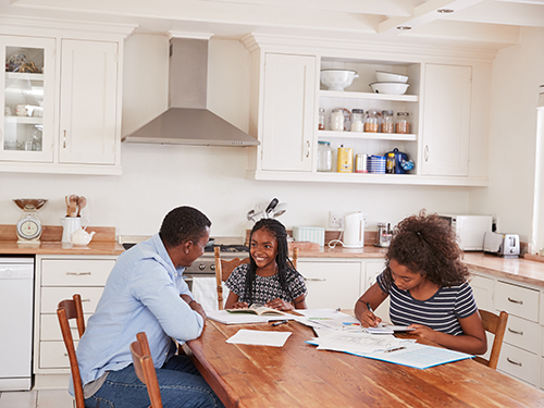 father and daughters doing homework at kitchen table