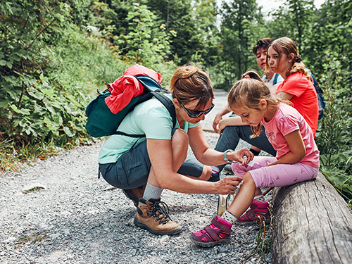 parent fixing girls knee injury during family hike