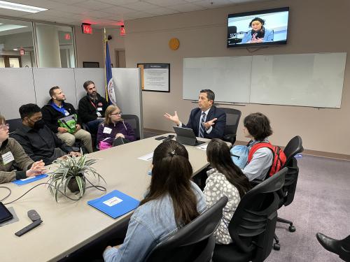Students sit at a conference table and learn about the Office of Public Affairs.