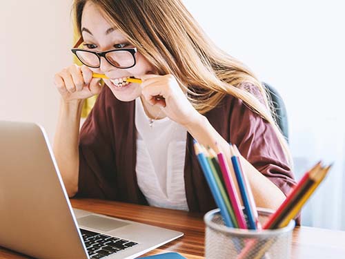 person looking at laptop biting pencil