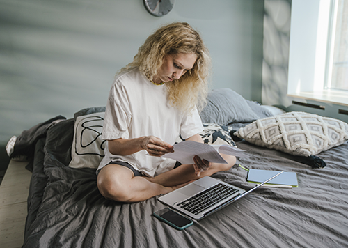 woman sitting on bed with open laptop and papers