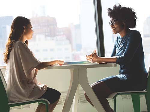 two people sitting at table by window talking