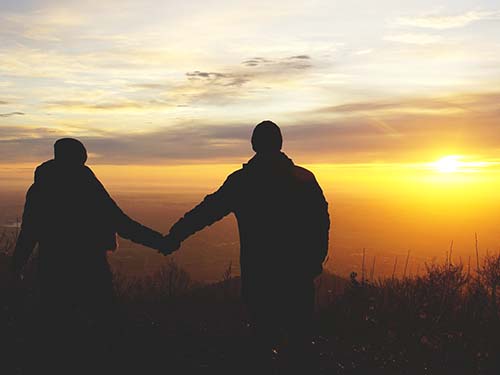 two people holding hands looking at sunset