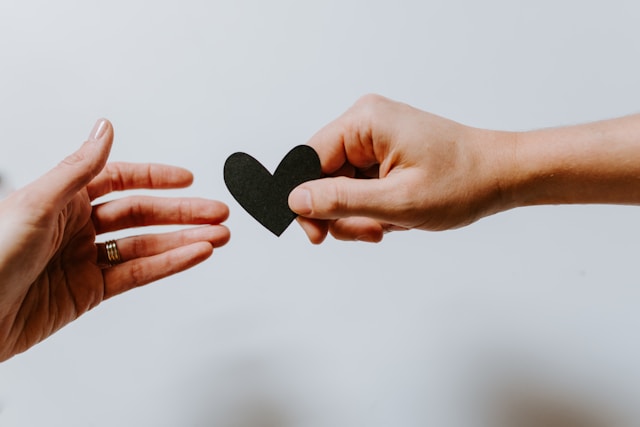 person reaching for black heart cutout paper