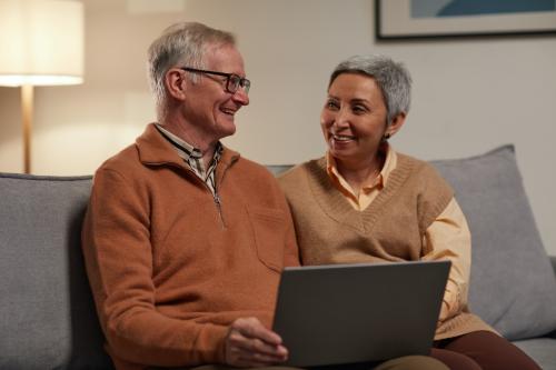 older couple sitting on couch with laptop looking at each other