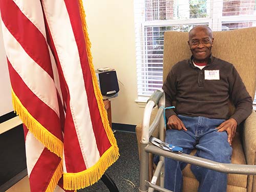 Bill Hawkins sitting in chair next to flag