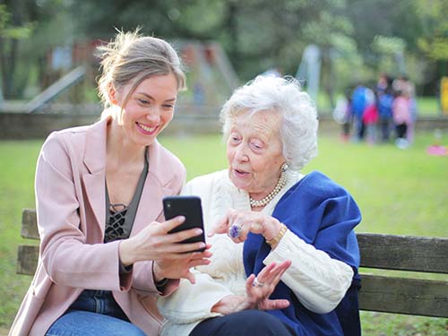 adult and older adult sitting on park bench viewing cell phone