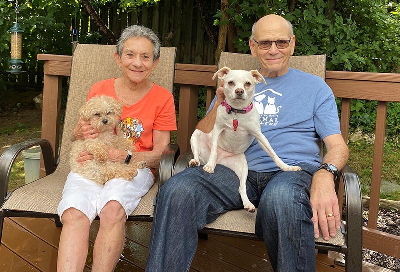Photo of Barry and Rita Altman sitting in their backyard with their two dogs.