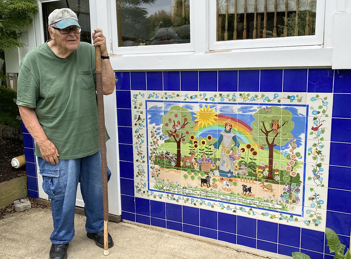 Photo of Joe Francis standing next to a tile mural on the back of his home.