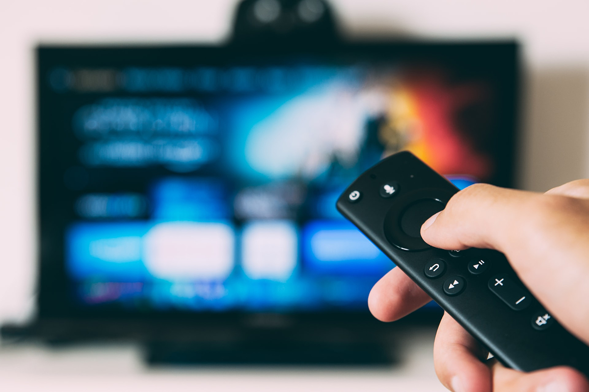 Photo of a hand holding a remote control and pointing it at a TV