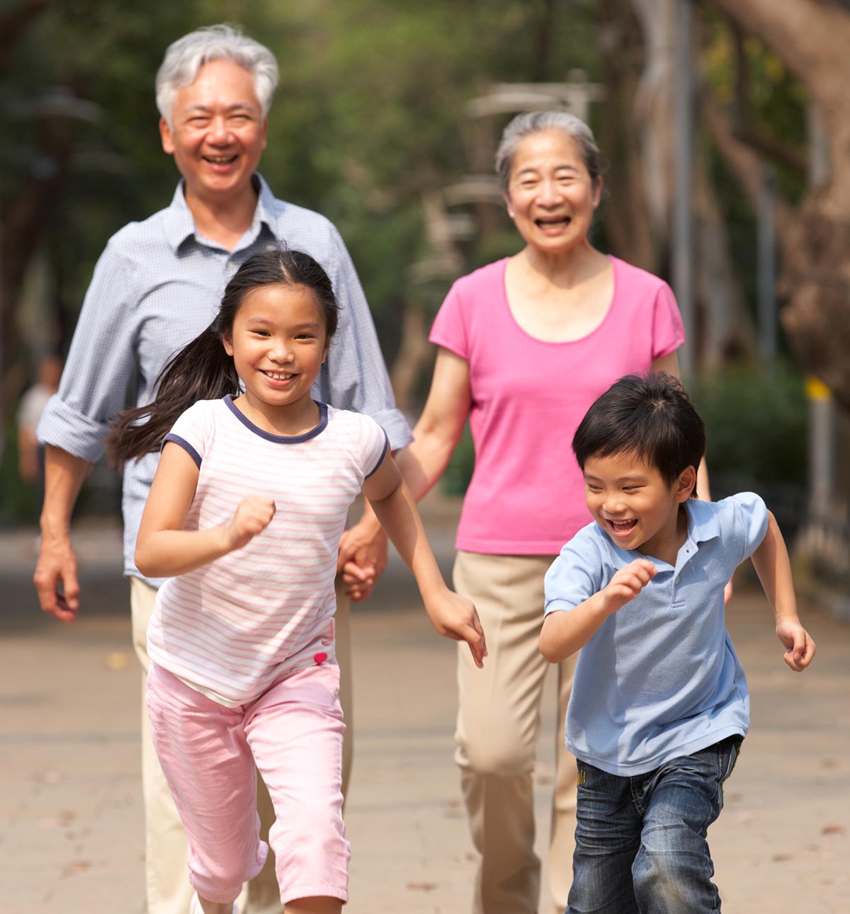 Photo of two happy children running on a path in front of their grandparents.