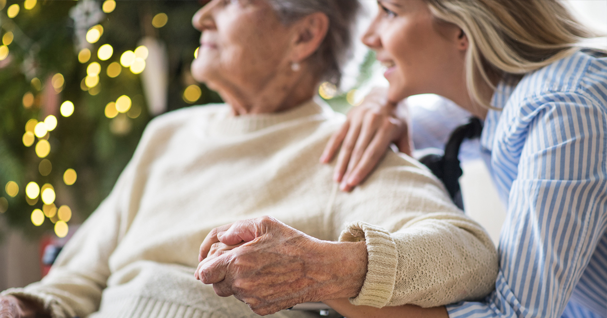 Photo of a younger woman holding an older woman's hand with holiday lights in the background.