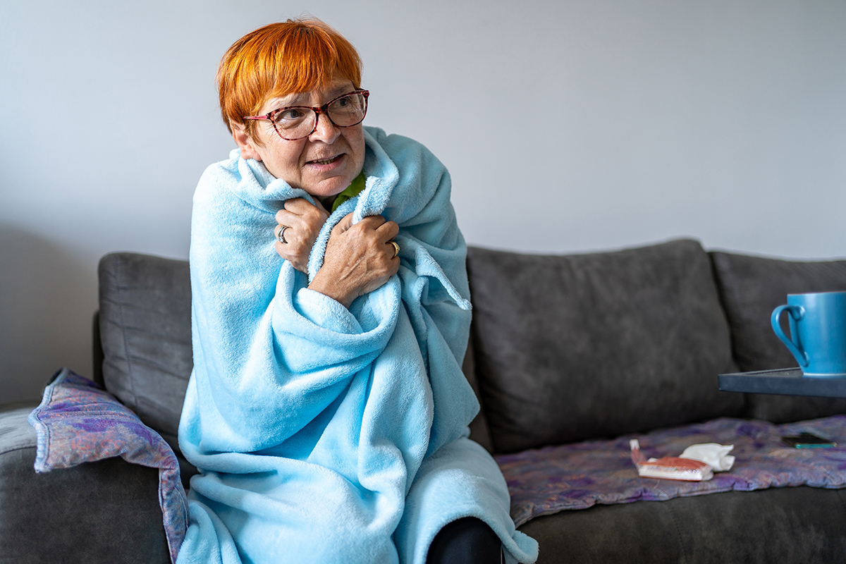Photo of a older woman sitting on a sofa draped in a blanket to stay warm