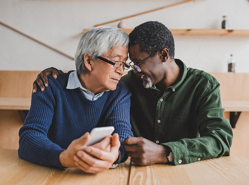 Photo of a an older Asian man and an older African American man embracing