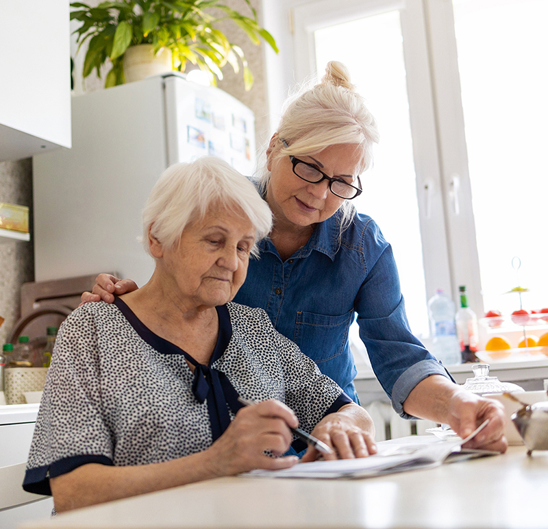 Photo of an adult woman helping an older adult woman with paperwork